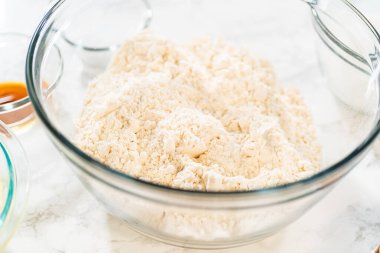 Klasik Şekerli Kurabiye Hamuru için, un ve şeker içeren kuru malzemelerle dolu bir karıştırma kabının açılı görüntüsü. Kase mermer bir tezgahın üzerine kurulmuş, yakınındaki konteynırlar da diğerini tutuyor.