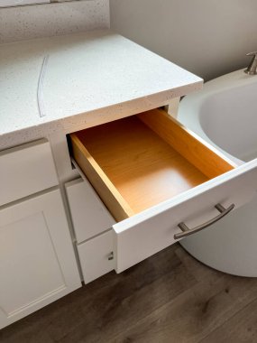 Castle Rock, Colorado, ABD-11 Şubat 2023 'te modern beyaz banyo makyaj dolabında kuvars tezgahı olan ahşap bir çekmeceye yakın çekim. Çekmecede parlak metal saplar ve tamamlayıcılar yer alıyor.