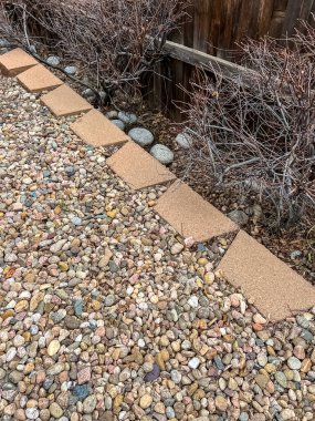 Değişik renk ve boyutlarda dekoratif taşlardan oluşan bir yatakla çevrili beton bloklardan oluşan yaşlanan bir istinat duvarının yakın görüntüsü. Manzara aşınma belirtileri gösteriyor ve hazır.