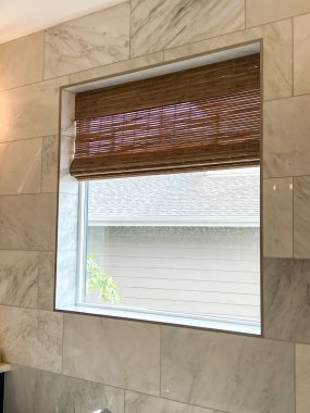 Modern bir pencere ayarında desenli Roma gölgelerine yakın çekim. Tarafsız kumaş ahşap desenli çerçeveyi tamamlıyor, uyumlu ve şık bir görünüm yaratıyor. Çağdaş ev dekorasyonu için mükemmel.