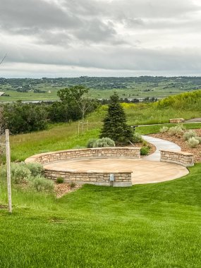 A view of a residential neighborhood in Castle Rock, Colorado, with homes overlooking an overgrown grassy landscape. The area features a winding path, scattered trees, and patches of wildflowers clipart