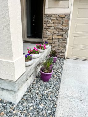 Verandanın kenarına yerleştirilmiş çiçek ve bitkiler hoş bir karşılama ve renkli bir açık hava alanı yaratıyor çömlekler çiçek ve yeşillik karışımı içeriyor.