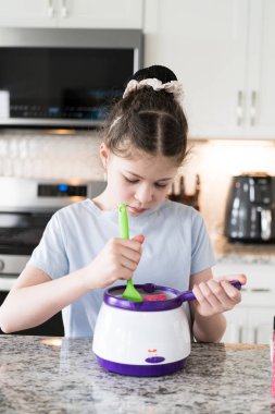 Odaklanmış bir dikkatle, bu filizlenen aşçılık sanatçısı krakerleri erimiş çikolataya batırarak iyi aydınlatılmış bir ev mutfağının sıcaklığında tatlı tatlar yaratıyor..