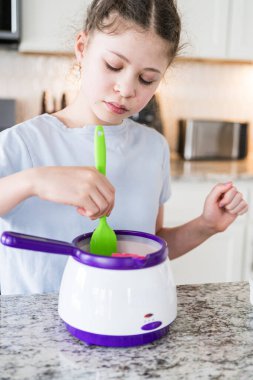 Odaklanmış bir dikkatle, bu filizlenen aşçılık sanatçısı krakerleri erimiş çikolataya batırarak iyi aydınlatılmış bir ev mutfağının sıcaklığında tatlı tatlar yaratıyor..