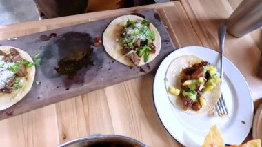 Castle Rock, Colorado, 12 Mayıs 2024 'te yavaş çekimde bir elin restoran masasındaki bir tabaktan taco alırken görüntüsü. Sahnede çeşitli renkli ve iştah açıcı yemekler var.