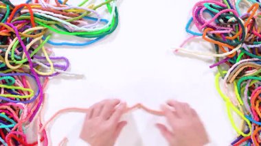 Düz yatıyordu. Eller birbirine zıt beyaz bir yüzeye karşı düzgün düzenlenmiş renkli, sarmalanmış kil boncuk iplikçiklerine dokunur..