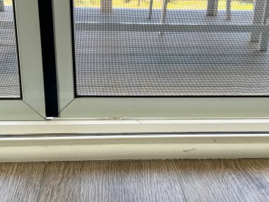 Çerçevesinde ve raylarında görünür hasar olan sürgülü bir kapının yakın plan görüntüsü. Alttaki pistte sürtünme izleri ve küçük çatlaklar görülürken, ekran kapısının çerçevesinde küçük bir göçük var. Döşeme