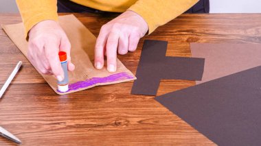 Adım adım. Öğretmen, kahverengi bir çantadan kağıt bir kukla yaparak, çalışma alanı olarak ahşap bir yüzey kullanarak çevrimiçi sınıfa rehberlik ediyor..