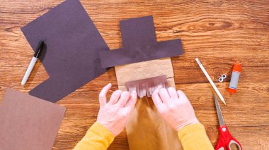 Adım adım. Düz yatıyordu. Öğretmen, kahverengi bir çantadan kağıt bir kukla yaparak, çalışma alanı olarak ahşap bir yüzey kullanarak çevrimiçi sınıfa rehberlik ediyor..