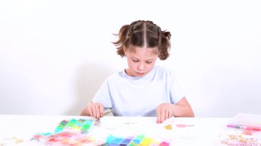 Genç kız derinden bilezik yapma sanatına odaklanmış. Canlı kil boncukları eşsiz kalıplara döküyor. Çalışma alanı çeşitli boncuklarla düzenlenmiş. Bu da nişanını gösteriyor.
