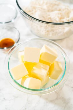 Close-up view of cubed butter in a glass bowl, ready for use in the Classic Sugar Cookie Dough recipe. The background features a mixing bowl with dry ingredients, hinting at the preparation steps for clipart