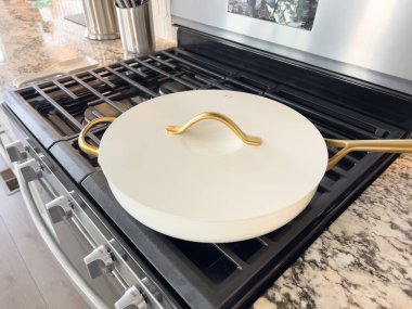 Castle Rock, Colorado, ABD-17 Ocak 2024-Altın saplı beyaz bir seramik tava modern bir mutfakta bir gaz sobasının üzerinde duruyor.