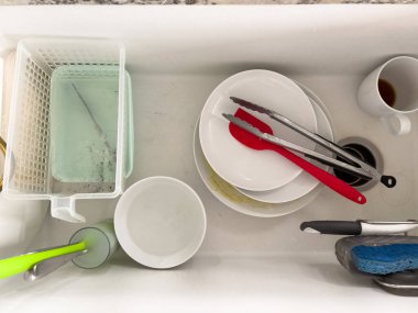 Castle Rock, Colorado, ABD-18 Ocak 2024-Tabaklar da dahil olmak üzere kirli tabaklarla dolu beyaz bir mutfak lavabosu maşa ve bıçak gibi kahve fincanları sabunlu suyla dolu bir bulaşık rafı