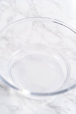 İçi su dolu geniş bir cam karıştırma kabı olgun çilekleri nazikçe temizlemek için hazır bekliyor. Kurumadan ya da depolamadan önce el değmemiş olduklarından emin olmak için..