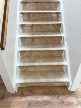 Tadilattan geçen bir merdiven. Tahta basamakları toz ve enkazla gösteriyor. Çevreleyen beyaz duvarlar ve yeni döşenmiş ahşap döşemeler devam eden bir ev geliştirme projesini gösteriyor.