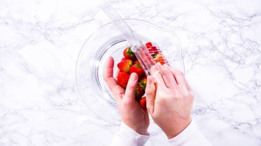 Düz yatıyordu. Olgun çilekler, depolama veya tüketimden önce temizlik ve uzun ömürlü olmak için meyveyi yıkamada bir adım olarak büyük bir bardakta karıştırma kabında suya gömülür..