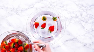 Düz yatıyordu. Olgun çilekler, depolama veya tüketimden önce temizlik ve uzun ömürlü olmak için meyveyi yıkamada bir adım olarak büyük bir bardakta karıştırma kabında suya gömülür..