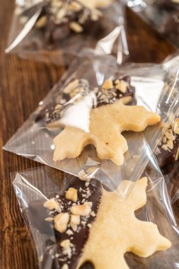 Dikkatlice paketlenmiş Noel kurabiyeleri, çikolataya batırılmış ve şeffaf selofan ambalajla sunulmuş, bayram hediyesi olarak mükemmel..