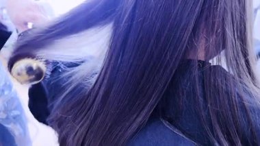 Nazik eller saç kurutma makinesini yeni kesilmiş genç bir kızın üzerinden geçirir ve titiz bir şekilde kestikten sonra kurutma işlemini gösterir. Kurutucunun sıcaklığı onun kilitlerine hayat veriyor.