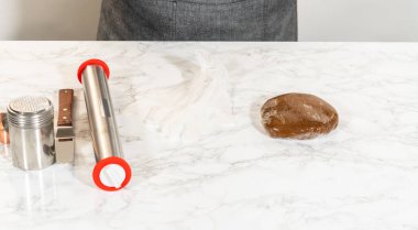 Mermer tezgahın üzerine yerleştirilmiş baharatlı zencefilli kurabiye hamuru ve merdane pimi ve süzgeç gibi fırınlama aletleri, hazırlığa hazır..