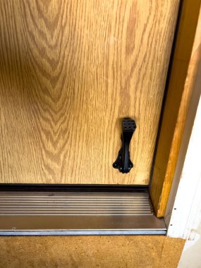 Altında siyah metal bir kirişin olduğu ahşap bir kapının yakın çekimi. Kapı metal bir eşik içine kurulmuş ve etrafındaki zemin desenli bir yüzeye sahip. Kickstand tutmak için kullanılır