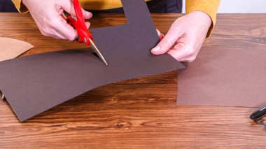 Adım adım. Öğretmen, kahverengi bir çantadan kağıt bir kukla yaparak, çalışma alanı olarak ahşap bir yüzey kullanarak çevrimiçi sınıfa rehberlik ediyor..