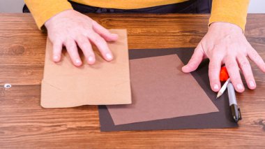 Adım adım. Öğretmen, kahverengi bir çantadan kağıt bir kukla yaparak, çalışma alanı olarak ahşap bir yüzey kullanarak çevrimiçi sınıfa rehberlik ediyor..