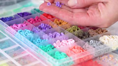 Parlak renkli balçık boncuklarından oluşan geniş bir koleksiyonu bölümlere ayıran eller, karmaşık malzemelerin güzelliğini ve çeşitliliğini vurguluyor.