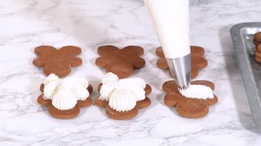 Zencefilli kurabiyeler mermer yüzeyde ikinci yarılarını beklerler, her biri lezzetli sandviçler yapmak için tereyağlı kremayla titizlikle borular. Boruların hassasiyeti şenlikli bir dokunuş katıyor..