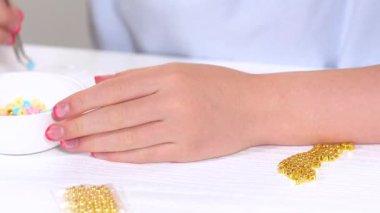 Genç kız derinden bilezik yapma sanatına odaklanmış. Canlı kil boncukları eşsiz kalıplara döküyor. Çalışma alanı çeşitli boncuklarla düzenlenmiş. Bu da nişanını gösteriyor.