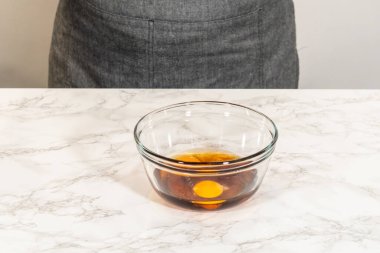 Mermer tezgahın üzerine yerleştirilmiş yumurta ve akçaağaç pekmezli küçük bir cam kasenin önü. Çikolata, zencefilli kurabiye ve çörek karışımına eklenmeye hazır..