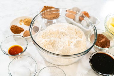 Çukulatalı Zencefilli Kurabiye Kurabiyesi Hamuru için baharat, tereyağı ve pekmez gibi diğer malzemelerle birlikte mermer bir yüzeye yerleştirilmiş elek ile dolu büyük bir cam karıştırma kabı..