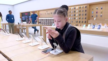 Denver, Colorado, ABD-9 Nisan 2024-10 yaşındaki bir kız dikkatle Apple Store 'daki bir stantta sergilenen yeni bir iPhone' u keşfediyor.