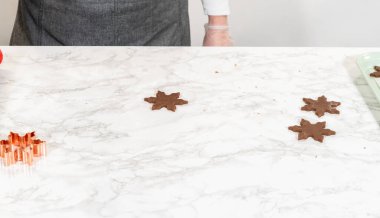 Üç tane kar tanesi şeklinde çikolatalı zencefilli kurabiye mermer bir yüzeyde kesilmiş ve pişirme tepsisine aktarılmaya hazır. Genel bakış açısı.