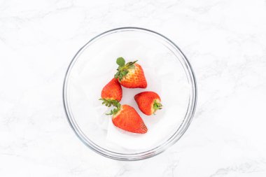 Parlak kırmızı çilekler, küf izleriyle karışmış, beyaz peçetedeki kağıt havluyla kaplı cam bir kasede dinleniyor, depolama tekniklerini gösteriyor..