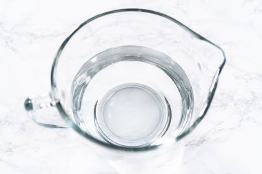 Cam ölçme bardakları suyla doludur, sıralanır ve dikkatli bir şekilde taze çilek yıkamada kullanılmaya hazırdır, kusursuz ve eksiksiz temizliği sağlar..