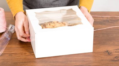 Tuzlu karamel şekerlemeleri ve zencefilli ekmek parçacıklarıyla süslenmiş zencefilli keki dikkatlice hediye etmek için açık pencereli beyaz bir kağıt bohça kek kutusuna yerleştiriyorum..