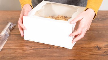 Tuzlu karamel şekerlemeleri ve zencefilli ekmek parçacıklarıyla süslenmiş zencefilli keki dikkatlice hediye etmek için açık pencereli beyaz bir kağıt bohça kek kutusuna yerleştiriyorum..