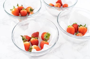 Parlak kırmızı çilekler, küf izleriyle karışmış, beyaz peçetedeki kağıt havluyla kaplı cam bir kasede dinleniyor, depolama tekniklerini gösteriyor..