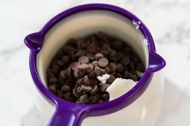 Çikolata parçacıkları ve tereyağı mor bir eritme kabına konmuş, zengin bir çikolata sosu yapmak için ısıtılmaya hazır..