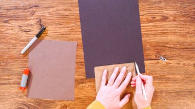 Adım adım. Düz yatıyordu. Öğretmen, kahverengi bir çantadan kağıt bir kukla yaparak, çalışma alanı olarak ahşap bir yüzey kullanarak çevrimiçi sınıfa rehberlik ediyor..