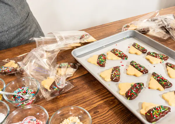 Dikkatlice paketlenmiş Noel kurabiyeleri, çikolataya batırılmış ve şeffaf selofan ambalajla sunulmuş, bayram hediyesi olarak mükemmel..