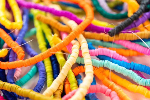 Beyaz bir masadaki renklere göre düzenlenmiş canlı bir kil boncuk koleksiyonu genç zanaatkarlara kendi eşsiz bileziklerini yapmaları için ilham vermeye hazır..