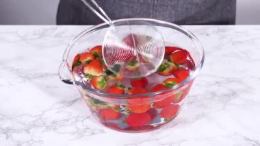 Olgun çilekler, depolama veya tüketimden önce temizlik ve uzun ömürlü olmak için meyveyi yıkamada bir adım olarak büyük bir bardakta karıştırma kabında suya gömülür..