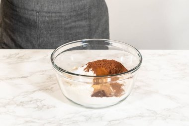 İçinde kakao tozu, baharat ve un içeren kuru çikolatalı zencefilli kurabiye hamuru bulunan bir kase mermer tezgahta karıştırılmaya hazır..