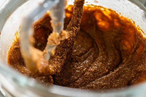 Karıştırıcı kasesinde kremalı tereyağı ve şekere eklenmiş koyu bir pekmez var. Pekmez entegre olmaya başlıyor, koyu kahverengi, aromatik bir karışım oluşturuyor..