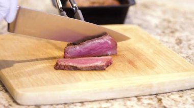 Eldivenli şef lezzetli pembe bifteği doğal bambu tahtasında, mutfak zemininde dilimliyor..