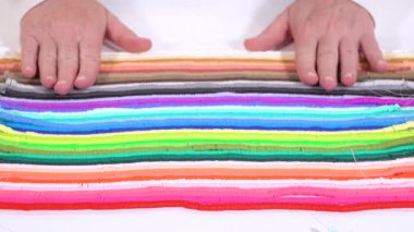 Eller birbirine zıt beyaz bir yüzeye karşı düzgün düzenlenmiş renkli, sarmalanmış kil boncuk iplikçiklerine dokunur..