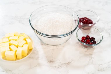 Pişirme tarifi için gerekli malzemelerin genel görünümü, küp tereyağı, bir kase çok amaçlı un ve taze yaban mersini. Tereyağı düzgün bir şekilde küp şeklinde düzenlenirken, un...