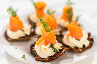 Çıtır bir krakerin üzerine zarif bir şekilde yerleştirilmiş füme somon kanalı. Üstünde krem peyniri, taze kekik ve zeytinyağı var. Canlı portakal somonu kontrastları